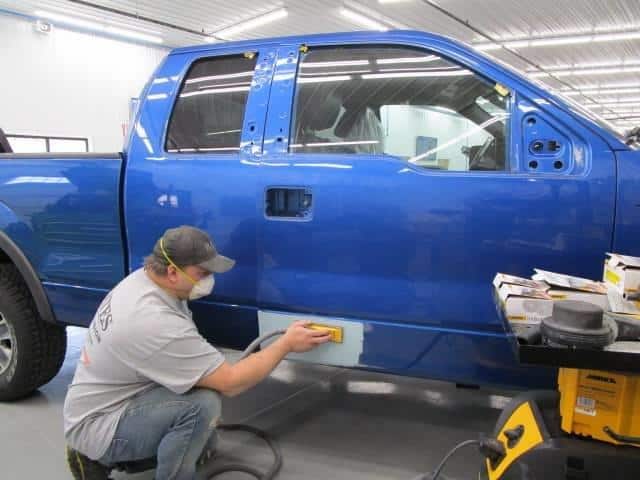 a technician repairing the side of a blue Ford truck at Bates Collision
